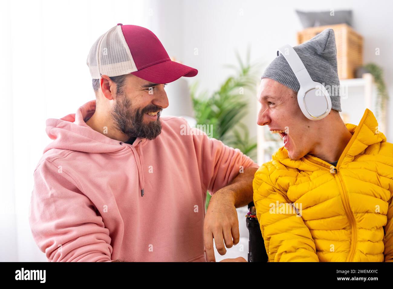 Excited disabled man listening to music using headphones with friend at home Stock Photo