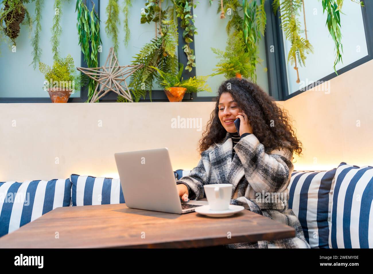 Casual young businesswoman with curly hair working in a colorful cafeteria drinking coffee Stock Photo