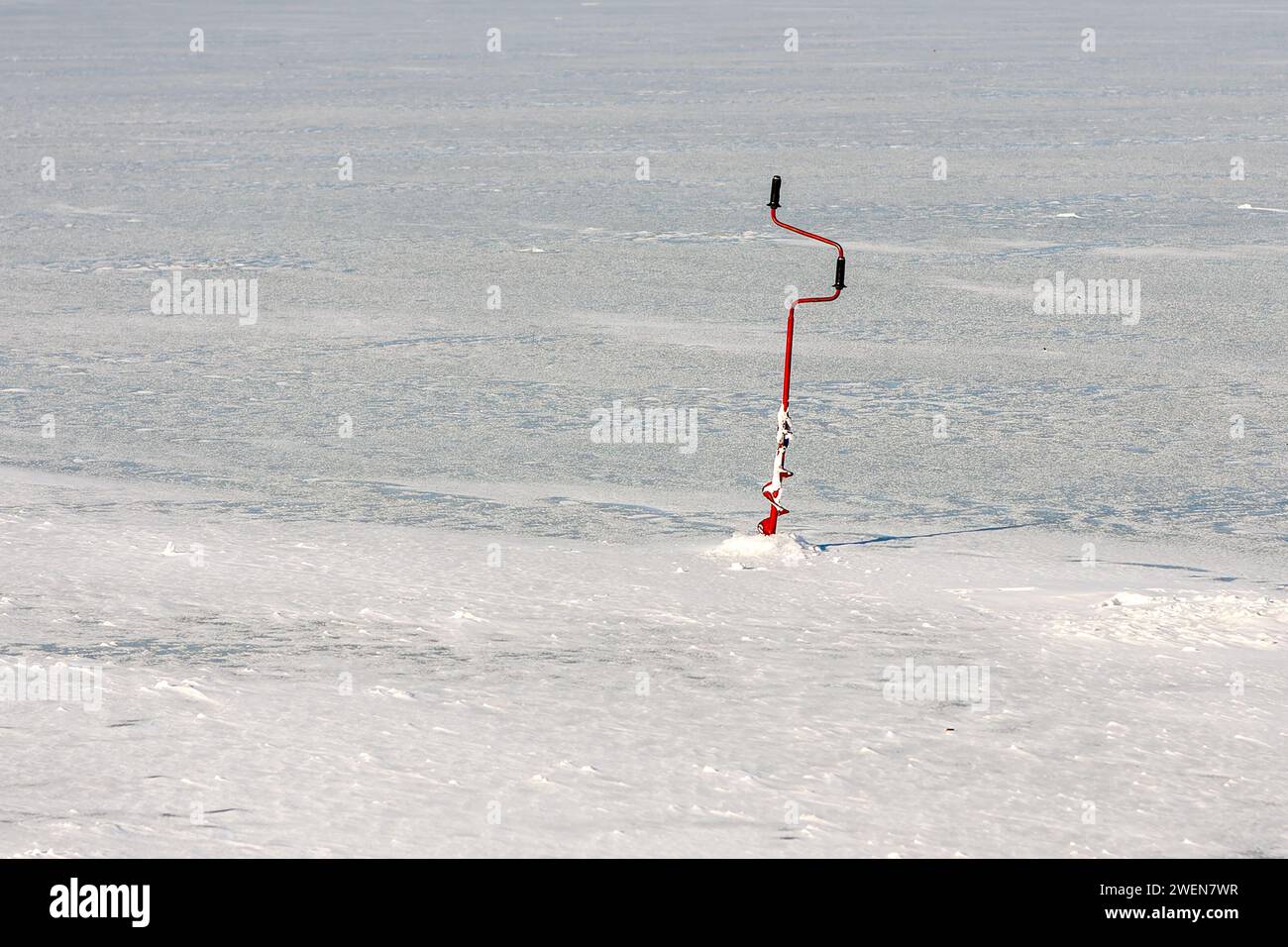 View of an ice drill in the lake ice. Drilling holes for winter fishing Stock Photo