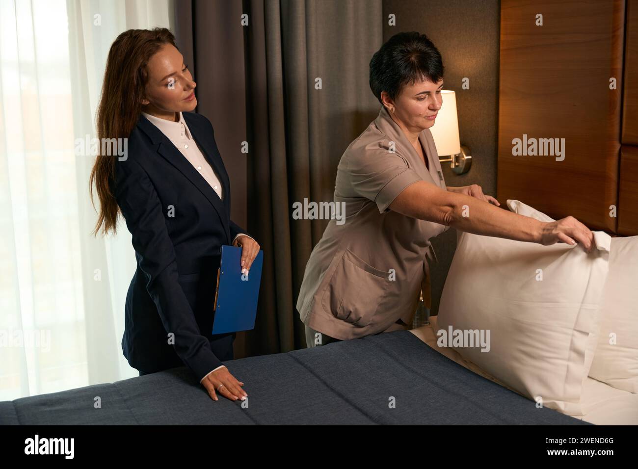 Maid supervised by hotel manager during bedmaking procedure in guest