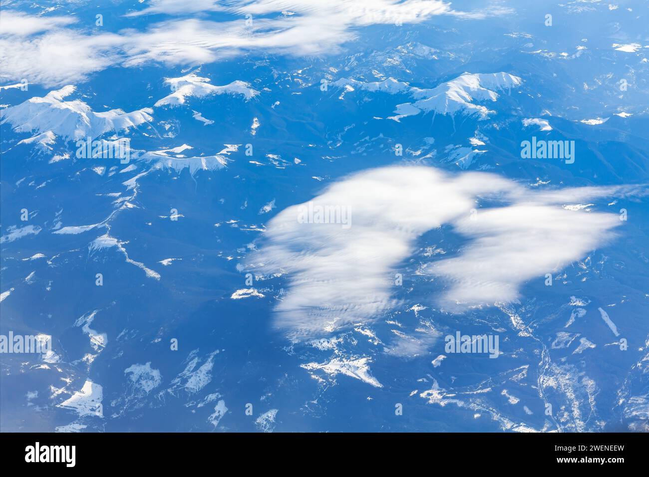 Clouds in the blue sky with snowy peaks as seen through window of an aircraft Stock Photo