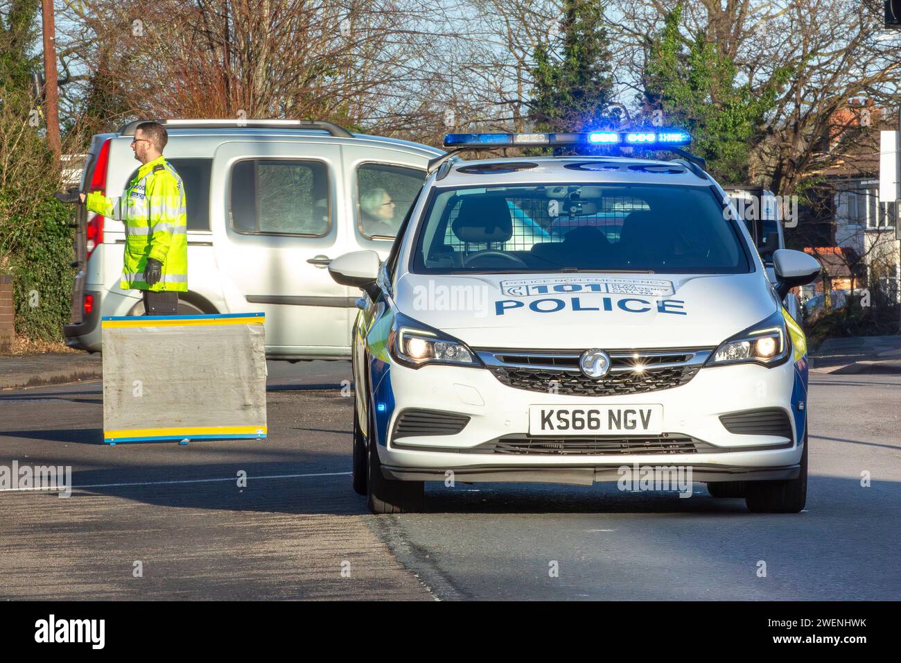 Front view of a police car with flashing blue lights and a police man directing traffic behind the vehicle. Stock Photo