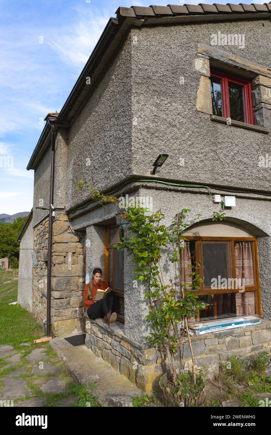 Woman sitting and reading at the entrance of a country house, vertical Stock Photo