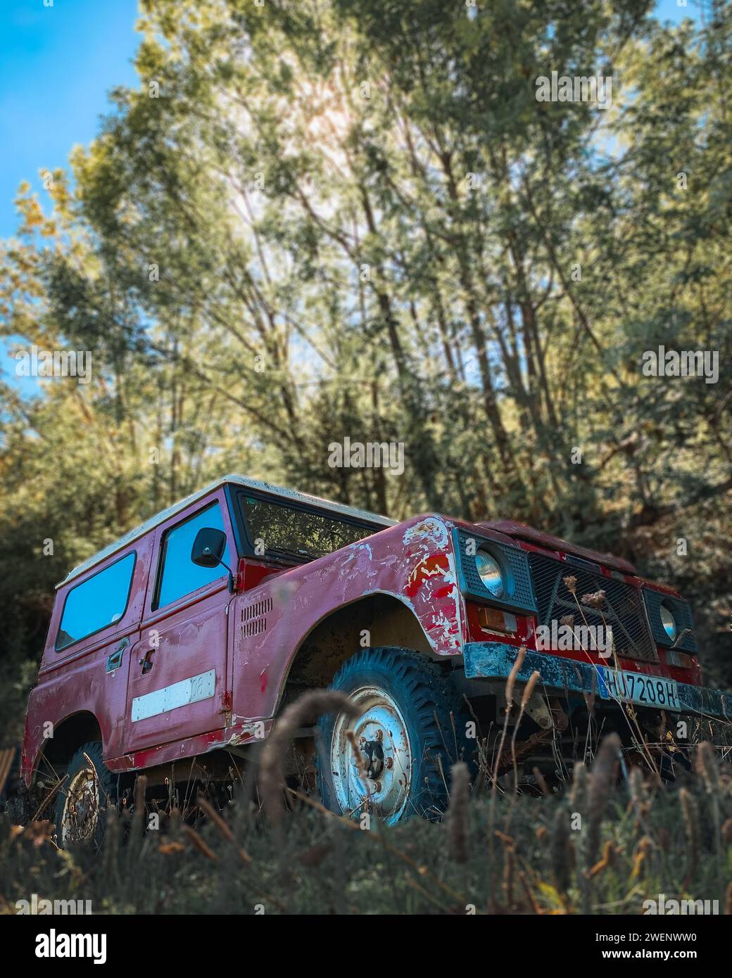 Vintage old red off-road car parked in the forest on a sunny day in middle of Pyrenees forest Stock Photo