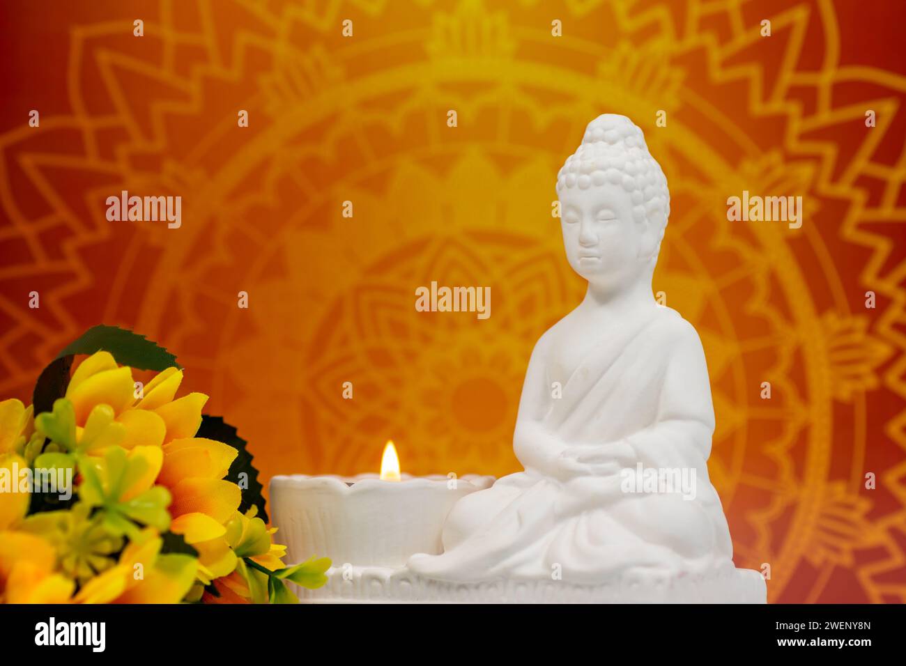 Close up of white marble figurine of Siddhartha Gautama, known as Buddha, with candle burning, decorative flowers, with colorful colorful background Stock Photo