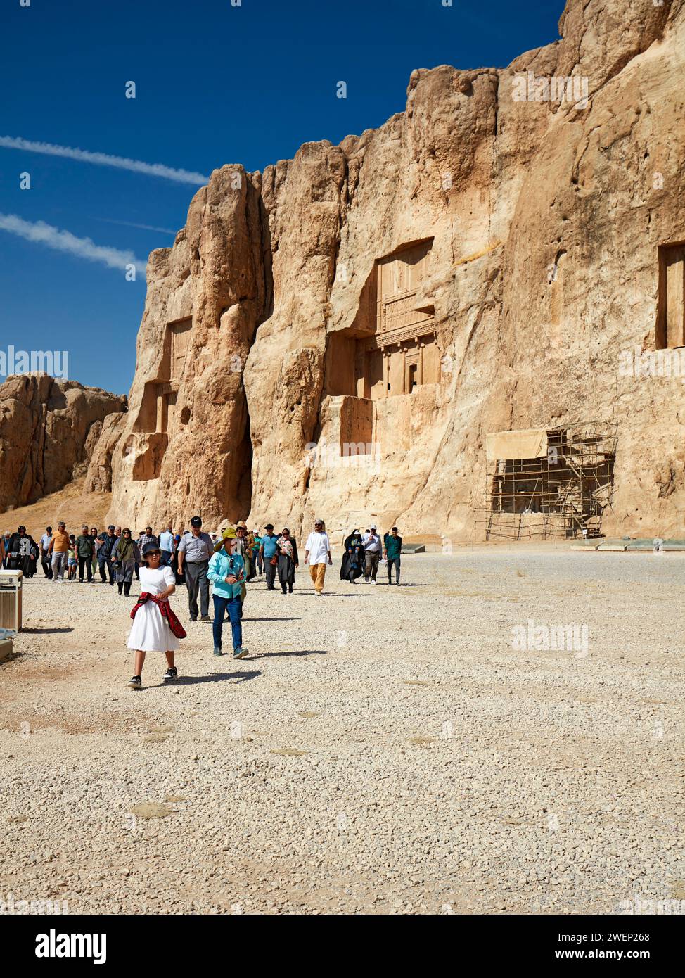 A group of tourists walk in Naqsh-e Rostam Necropolis, low rocky hill with rock-cut tombs of kings of Achaemenian dynasty near Persepolis, Iran. Stock Photo