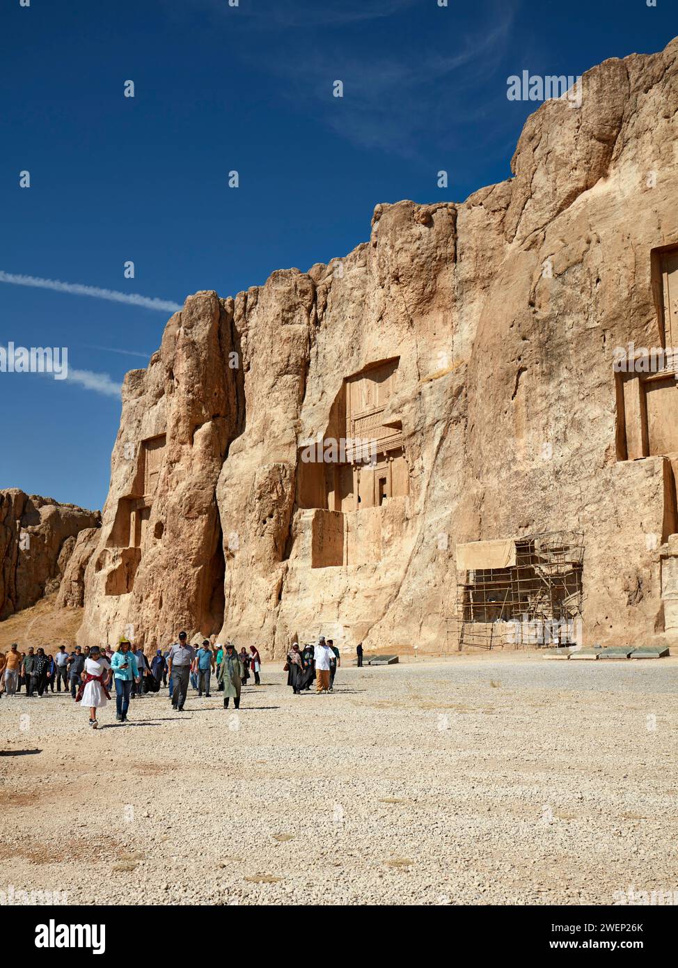 A group of tourists walk in Naqsh-e Rostam Necropolis, low rocky hill with rock-cut tombs of kings of Achaemenian dynasty near Persepolis, Iran. Stock Photo