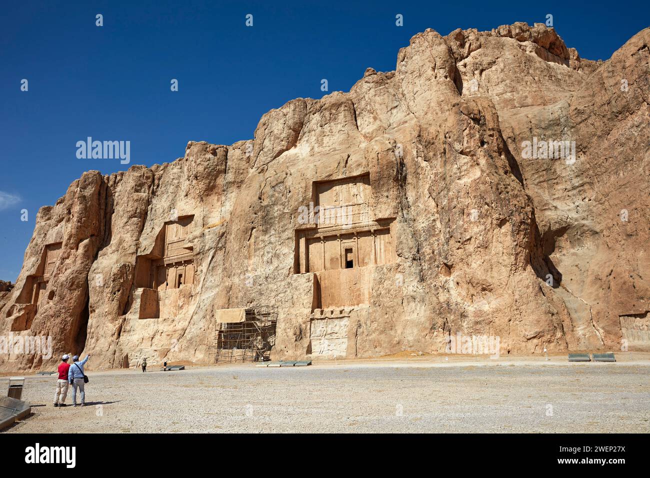 Tourists look at the rock-cut tombs of Persian kings of Achaemenid dynasty in Naqsh-e Rostam Necropolis near Persepolis, Iran. Stock Photo
