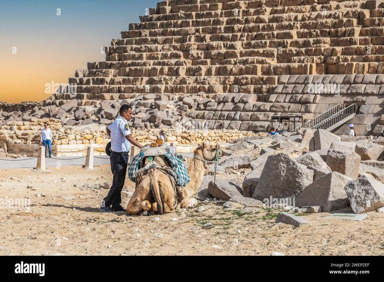 Giza Necropolis, Egypt - April 26, 2022:A policeman from the Tourist Police, visibly tired and warmed by the sun, is resting next to a camel with whic Stock Photo