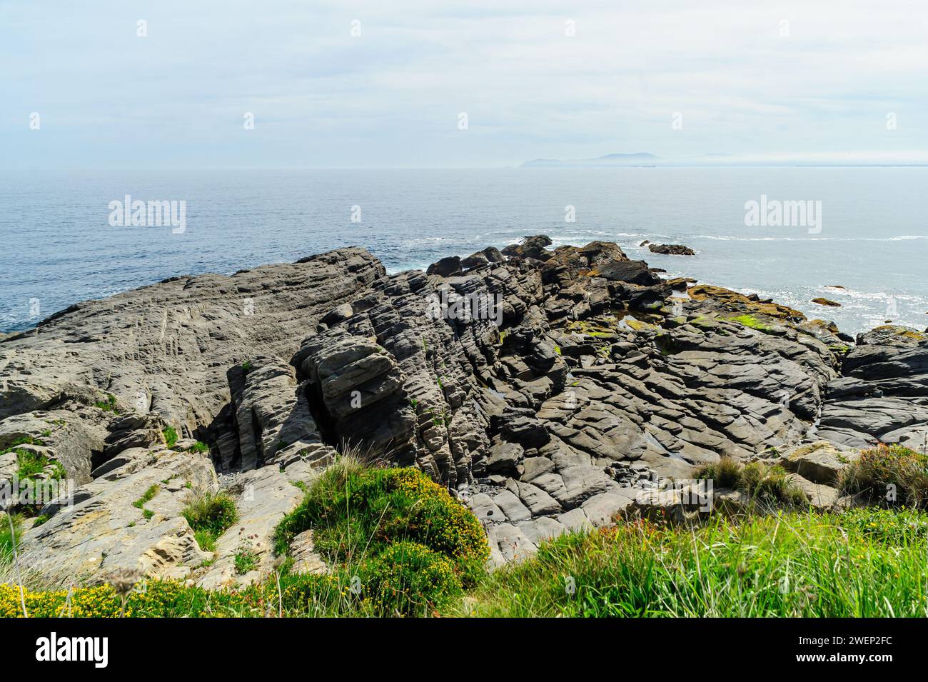 Striking layered rock formations along the rugged coast of Northern Spain with a clear blue sky overhead. Stock Photo