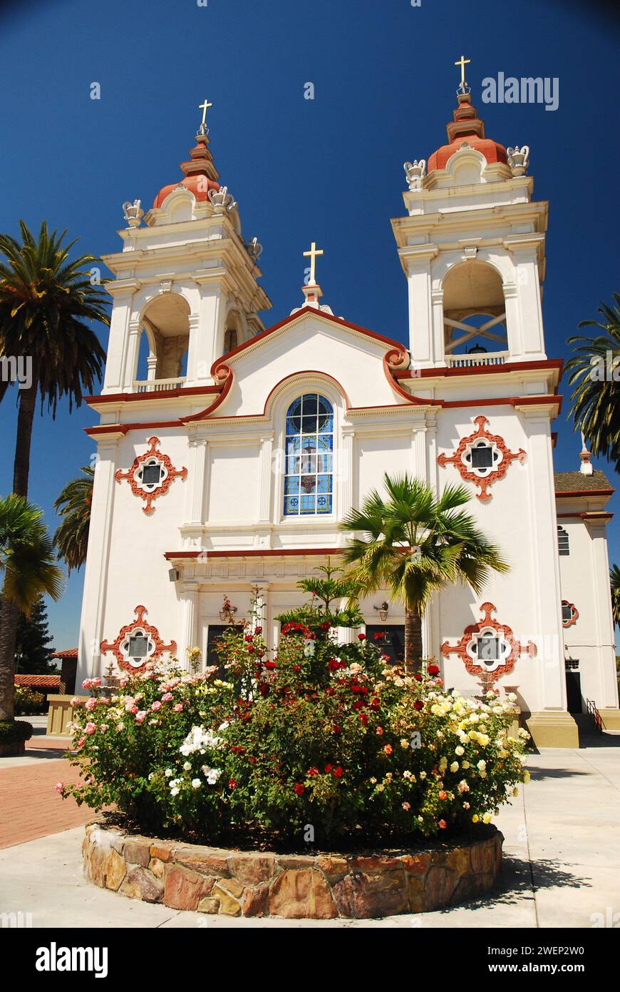 Flowers bloom and palm trees frame the historic Five Wounds Portuguese National Parish, a Catholic cathedral in San Jose California Stock Photo