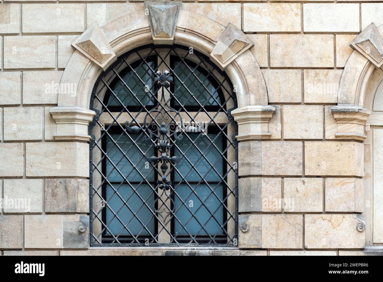 Arched window with wrought metal grille with pattern on the background of a beige colored stone block wall. From the windows of the world series. Stock Photo