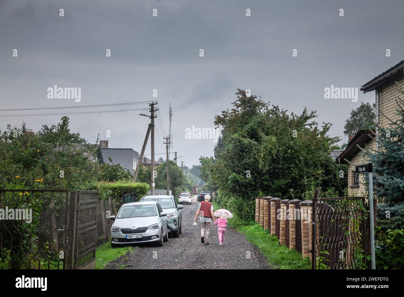 Picture of a rural street of Garciems, Latvia, with an old woman walking, holding her hand, with her grand daughter. Stock Photo