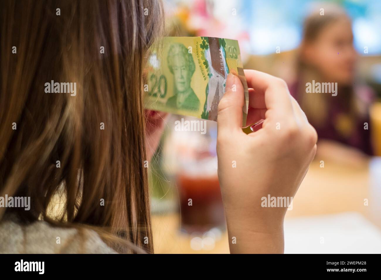 Helsinki, Finland - January 5, 2024: Girl investigating Canadian 20 dollar bill's security elements. Stock Photo