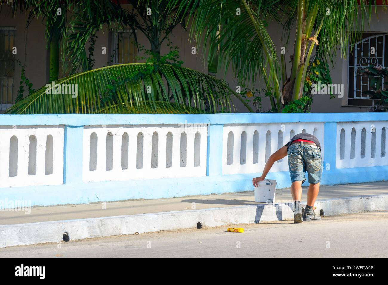 Man brush painting sidewalk curb, Santa Clara, Cuba Stock Photo