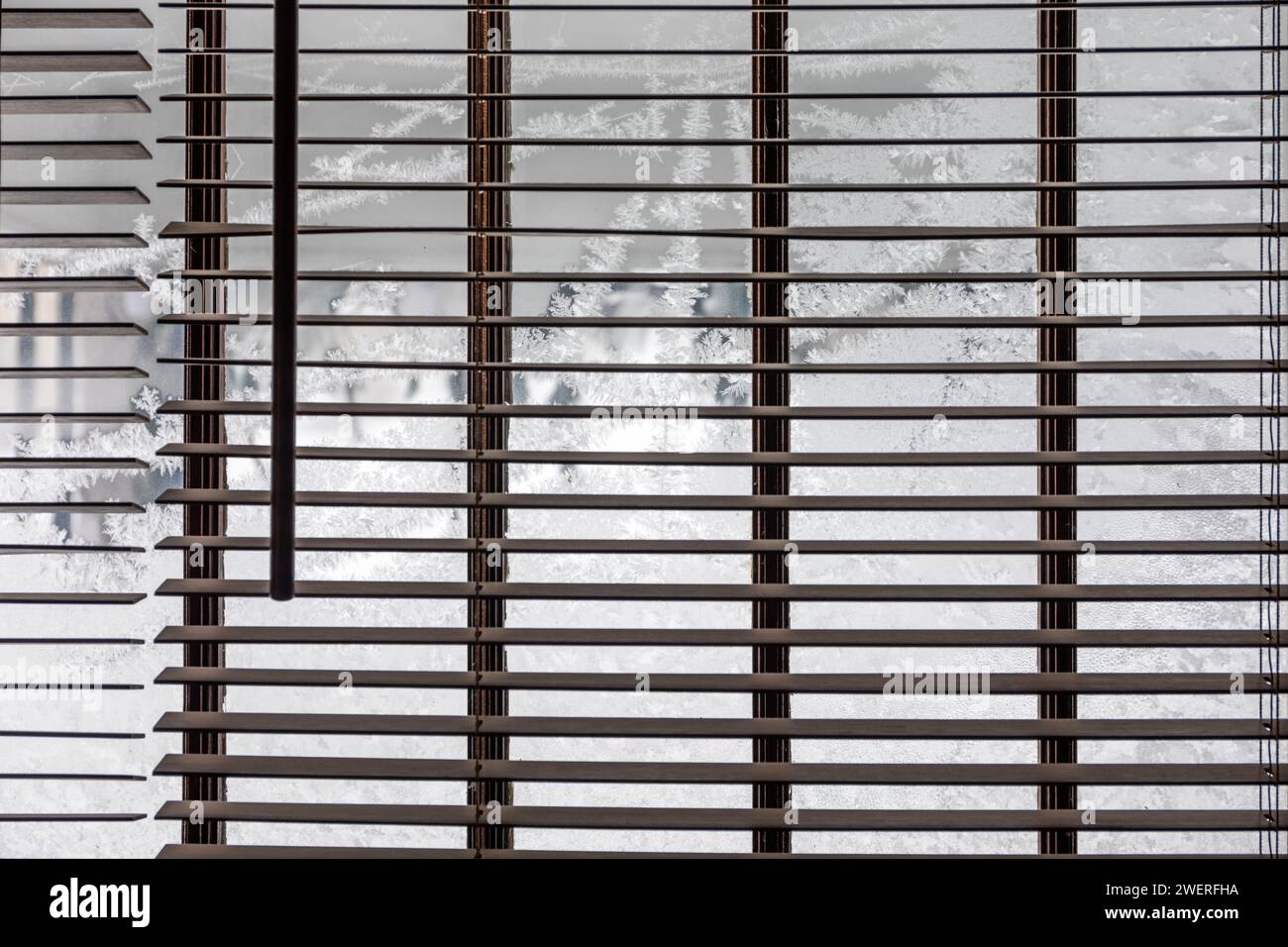 Ice crystals on window beyond venetian blinds. Stock Photo