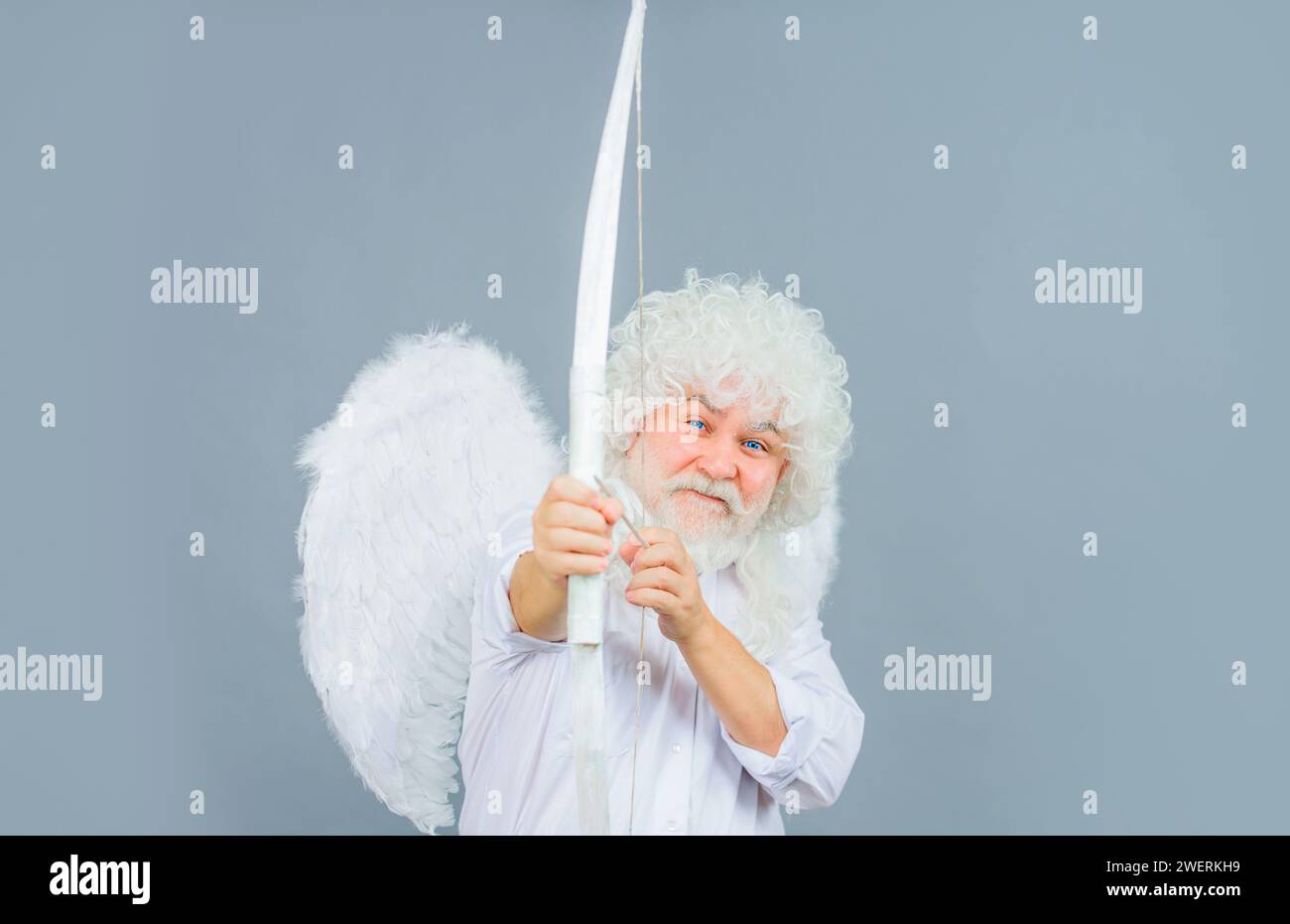 Valentines day. Smiling bearded man in angel costume aiming with bow. Male Valentine angel in white wig shoot arrow of love. Valentines day cupid in Stock Photo