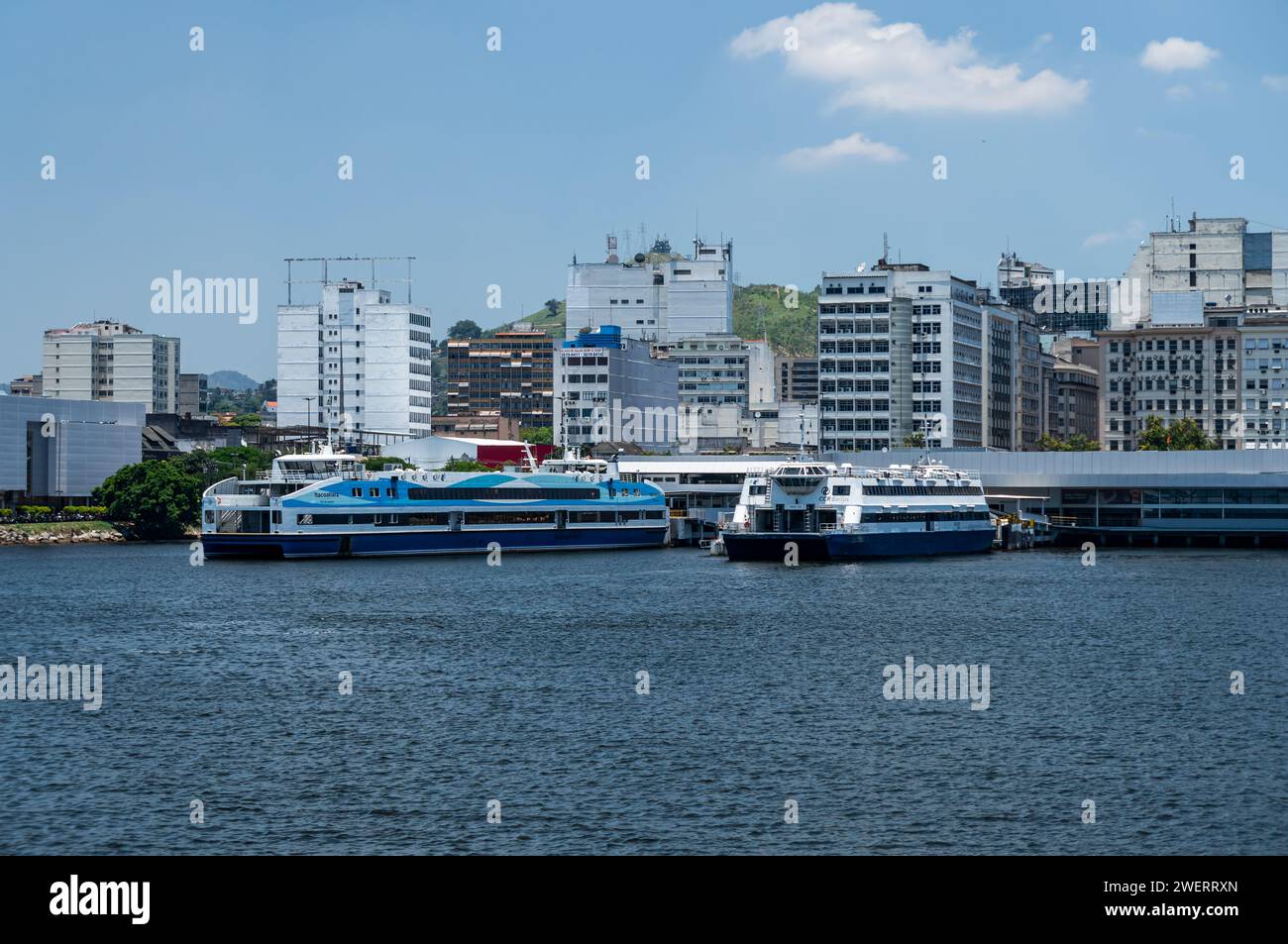 Ferry boats vessels docked at Arariboia ferry terminal in Niteroi Centro district as saw from Guanabara bay waters under summer afternoon blue sky. Stock Photo