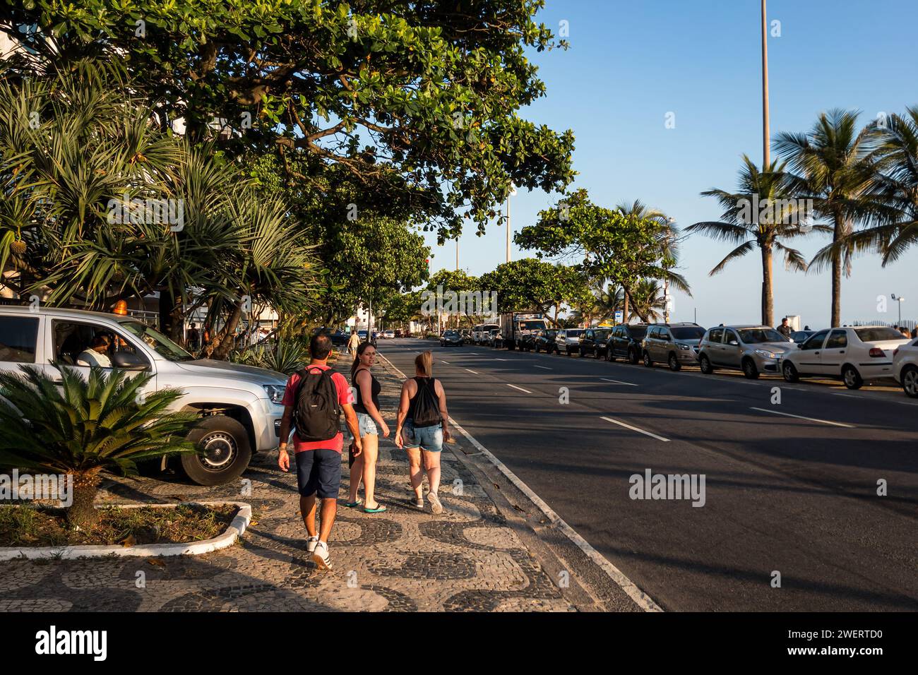 The cobblestone pavement sidewalk of Vieira Souto avenue full of green vegetation nearby the beach at Ipanema district under summer afternoon blue sky. Stock Photo