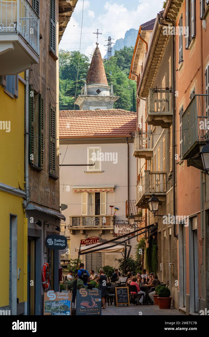 The steeple of the Church of Santa Marta can be seen rising beyond diners eating al fresco on the Via Cavour in Bellano, Lombardy, Italy. Stock Photo