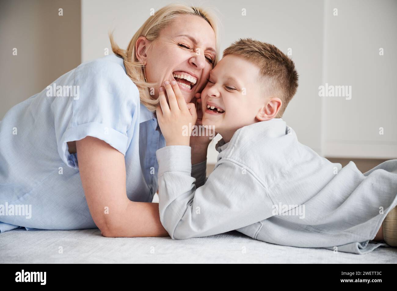 Joyful mom laughing with her son. Lovely moment of young mother and her kid smiling at home. Happy child having fun with his parent. Stock Photo