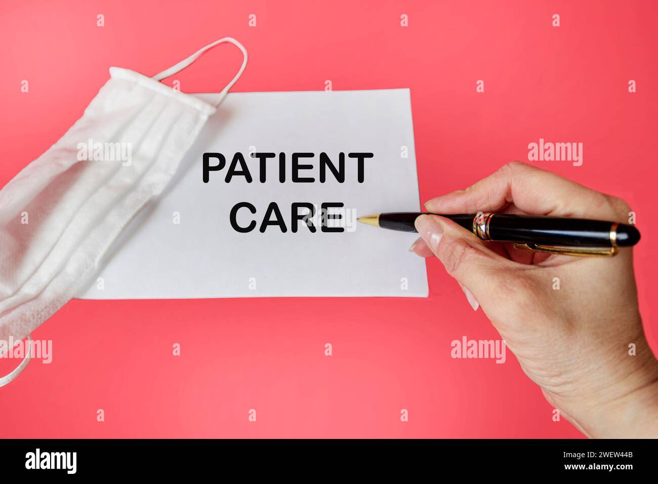 The text PATIENT CARE is written in a notebook by a doctor near a medical mask on a pink background. Medical concept Stock Photo