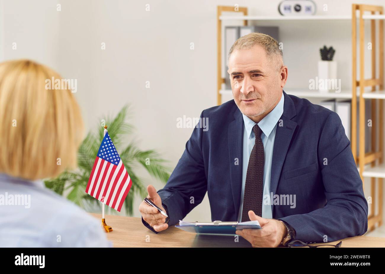 Woman sitting back in office of US public services or embassy and having visa interview. Stock Photo