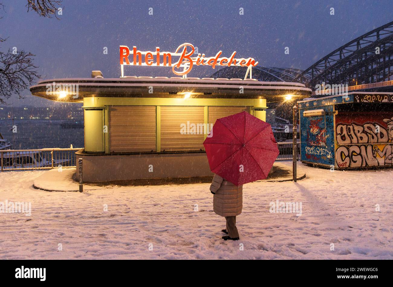 woman with umbrella standing in front of a closed kiosk on the snowy Rhine promenade near Hohenzollern bridge, snow, Cologne, Germany. 17.01.2024 Frau Stock Photo