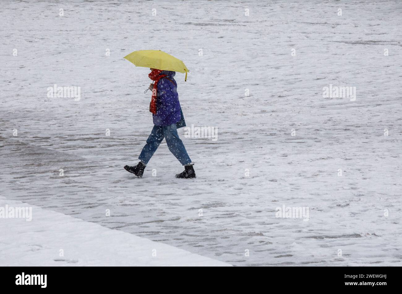 person with yellow umbrella walking across the station forecourt in snowfall, snow, winter, Cologne, Germany. Person mit gelben Schirm geht bei Schnee Stock Photo