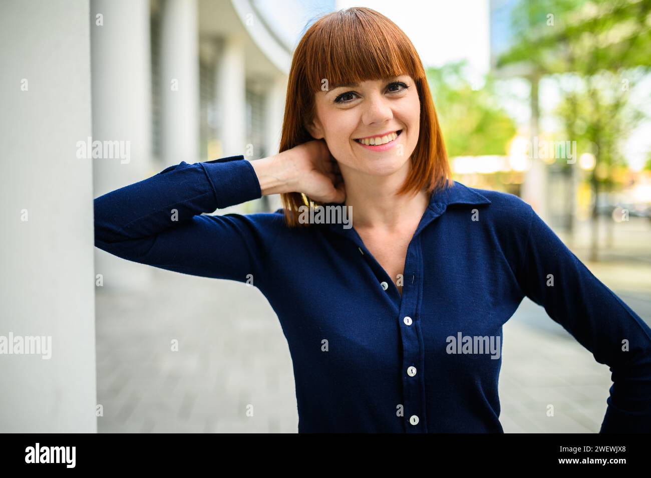 Attractive confident caucasian woman with casual clothing and elegant blouse. Smiling joyfully outdoors in an urban background Stock Photo