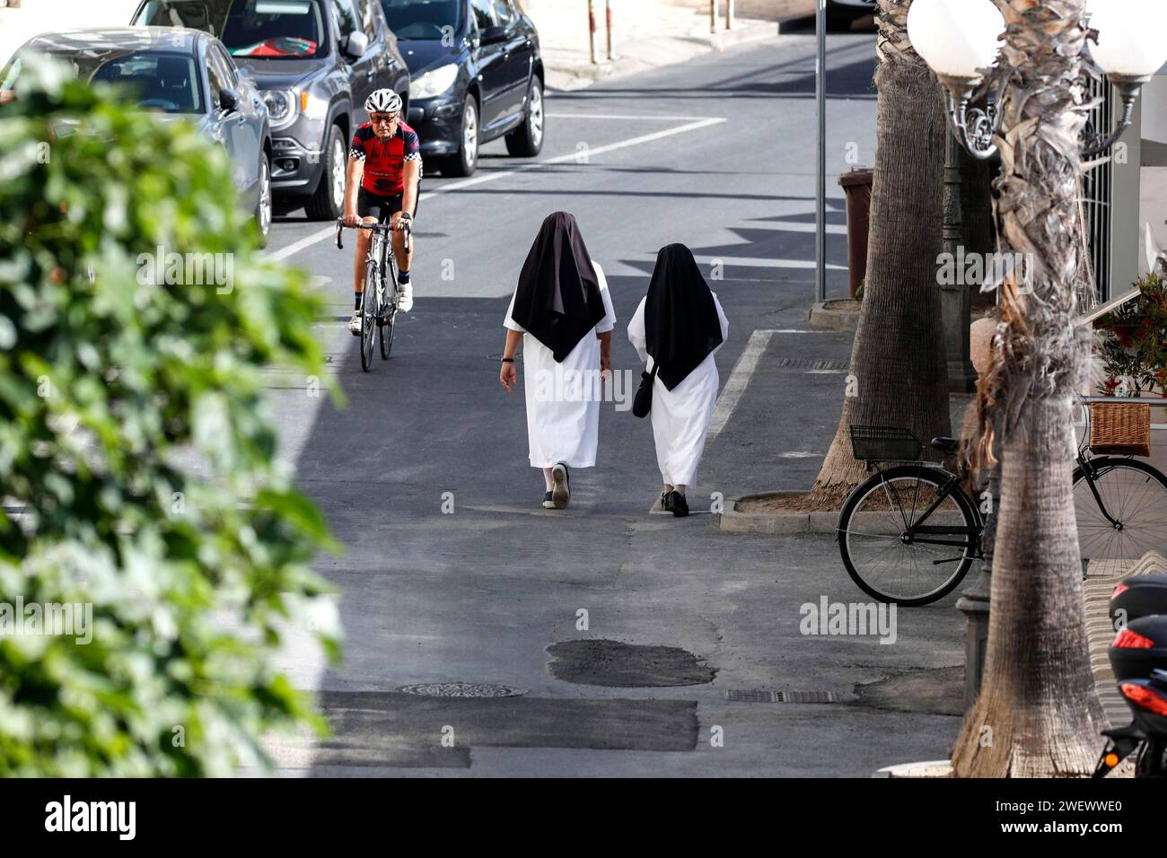 Two nuns walk across a street in Diana Marina, a man on a racing bike rides past, 28/05/2022 Stock Photo