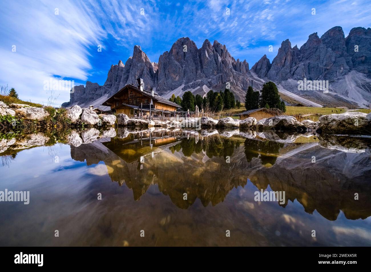 North faces and summits of Odle group and the mountain hut Geisler Alm, Rifugio delle Odle, reflected in a small pool. Bolzano Trentino-Alto Adige Ita Stock Photo
