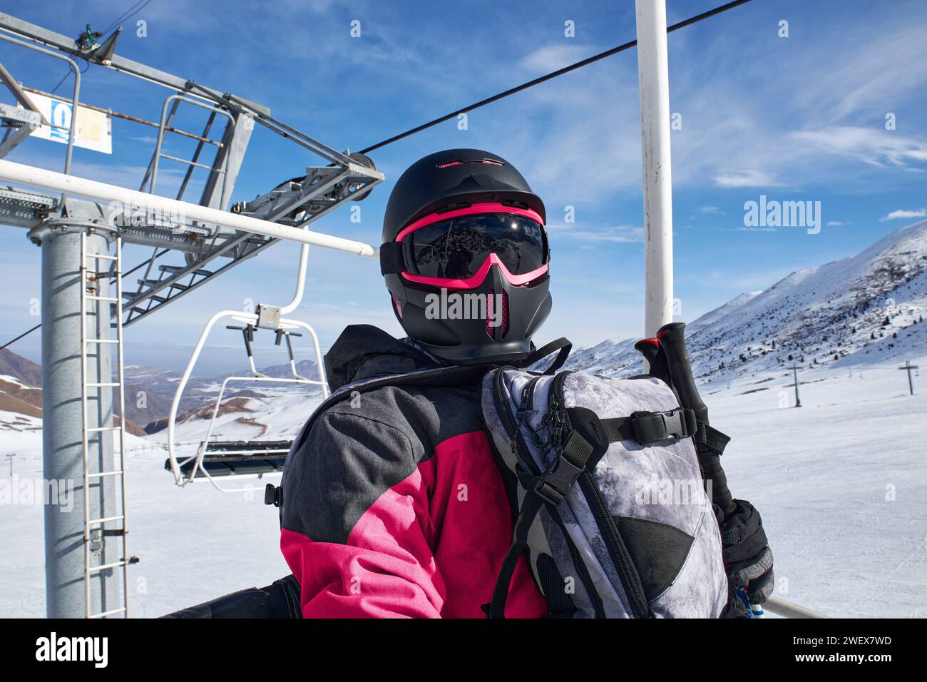 Man goes up ski lift. Person in snowboard equipment: stylish full face snow helmet black and pink color with goggles, backpack. Cable car construction Stock Photo