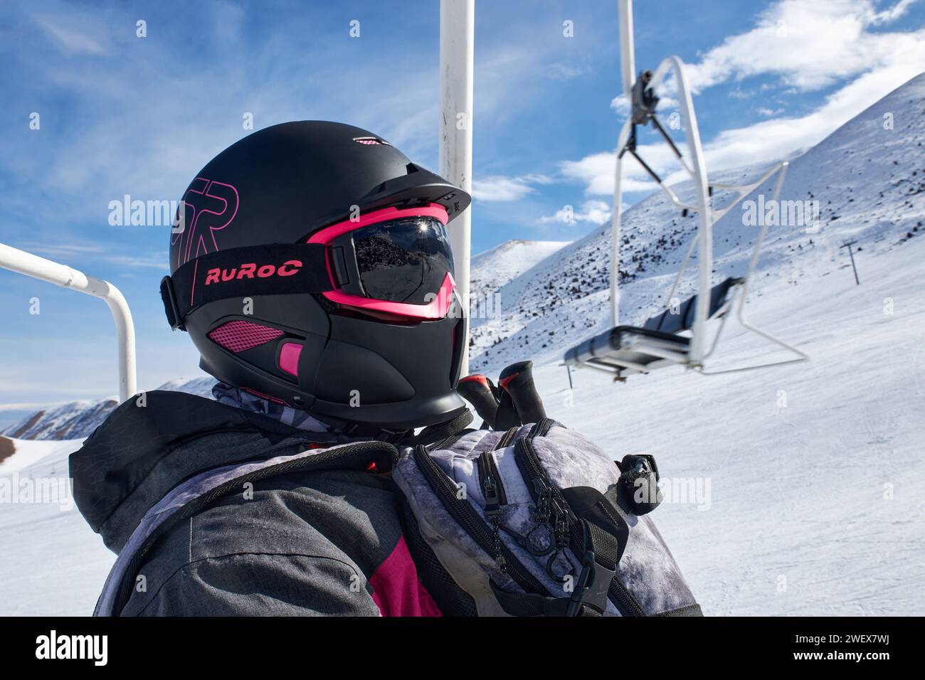 RuRoc stylish full face snow helmet black and pink color goggles. Man at ski cable car mountain lift, in snowboard winter equipment with backpack. Res Stock Photo