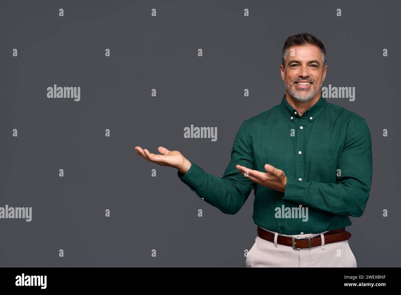 Smiling mature business man pointing aside advertising isolated on gray. Stock Photo