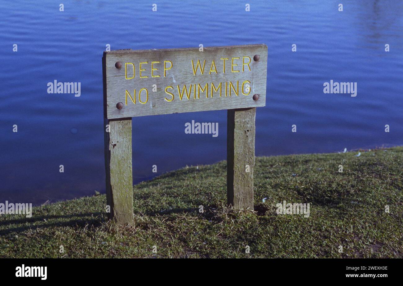 A wooden sign with carved lettering warning Deep Water No Swiming by the Needham Lake Needham Market Suffolk Stock Photo