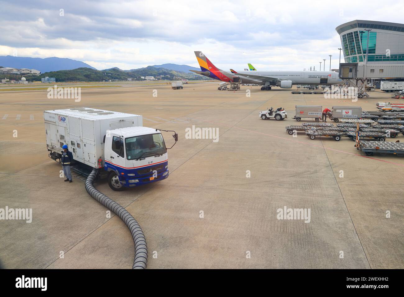 A ground supply power unit is attached to a modern airliner parked in an airport parking lot. Prior to flying, the aircraft undergoes maintenance and Stock Photo