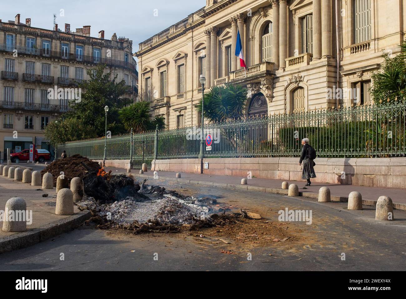 Montpellier, France, 2024. Place des Martyrs, a lady is looking at the fire still burning left by farmers protesting over unfair prices and taxes Stock Photo