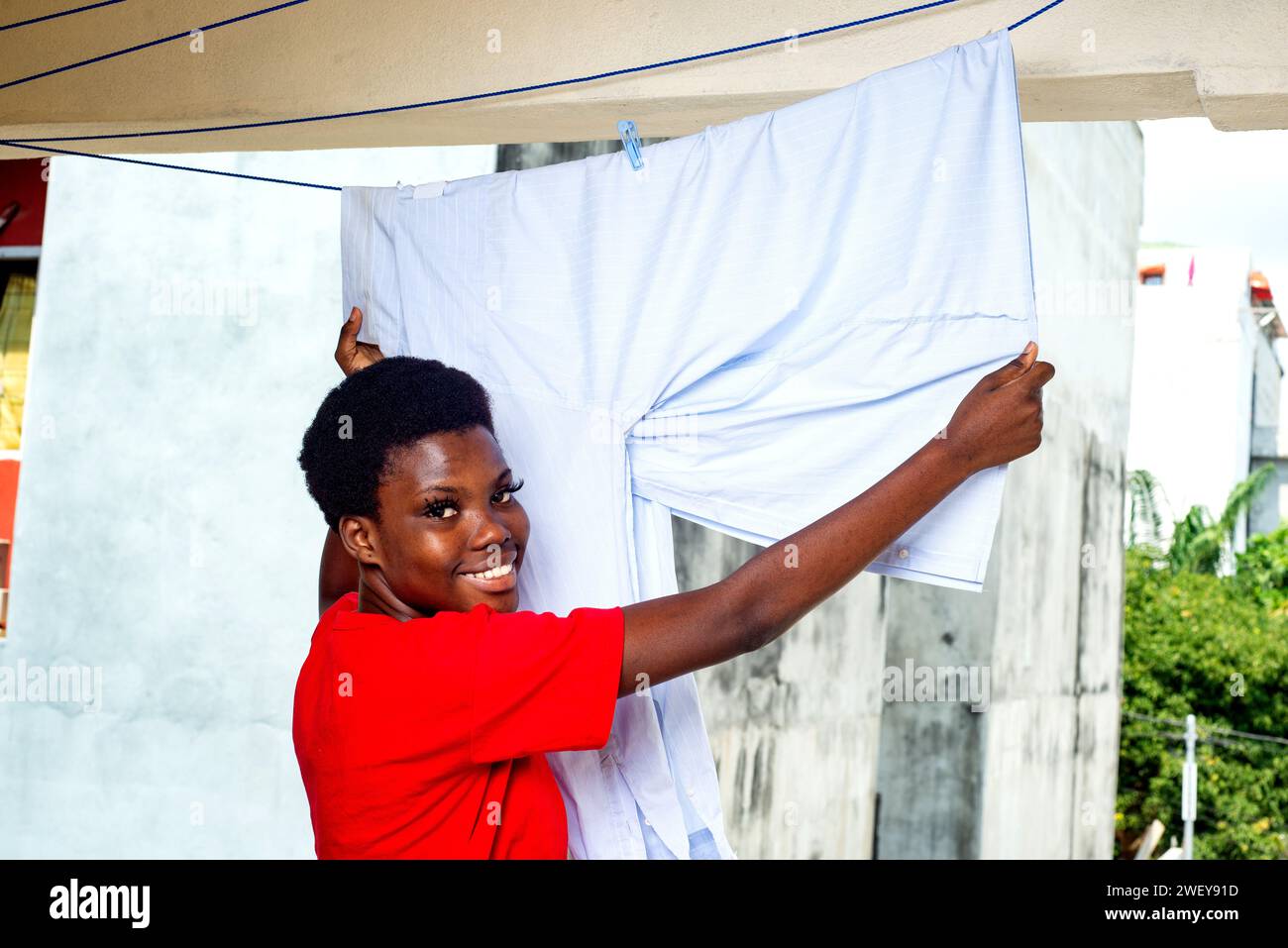 beautiful young girl drying a shirt on a clothesline on the balcony of the house while smiling. Stock Photo