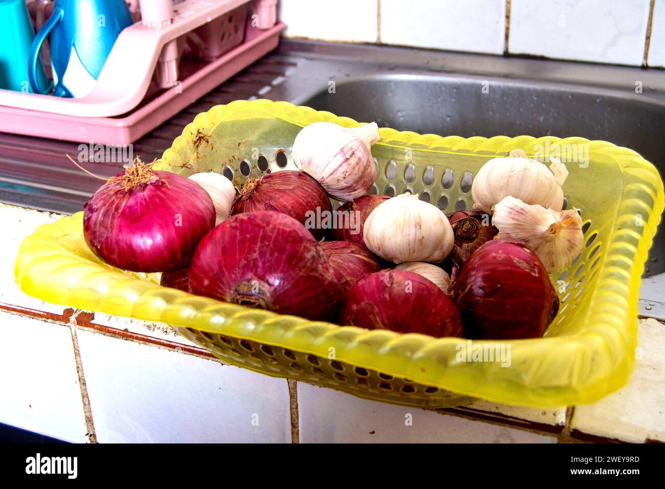 a basket on the kitchen sink containing onions and garlic. Stock Photo