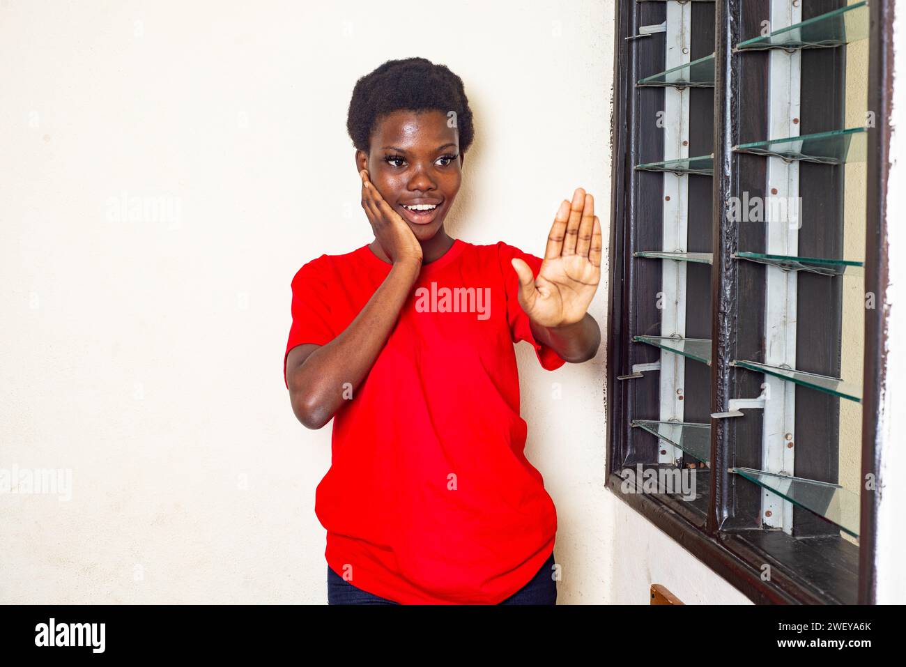 young beautiful woman in red t-shirt standing at home showing stop gesture smiling. Stock Photo
