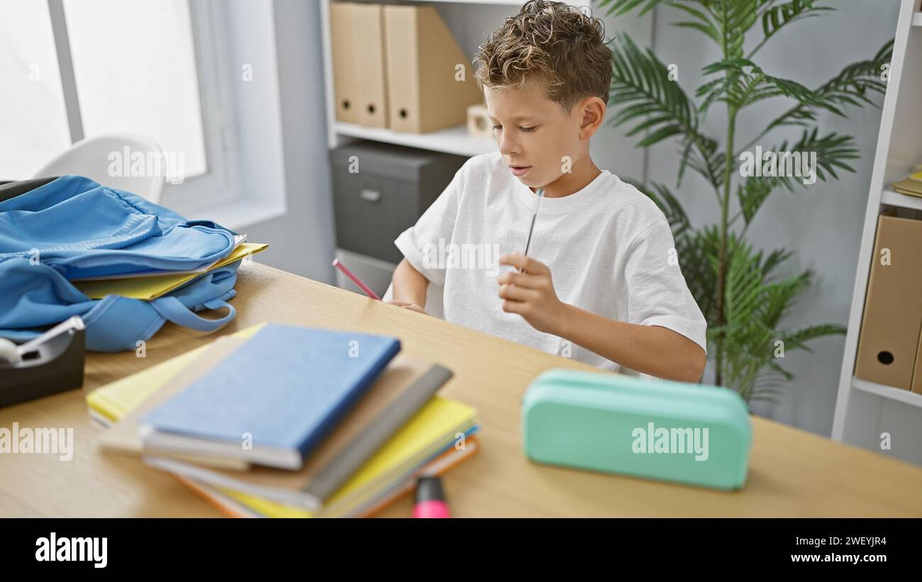 Adorable blond boy student delightfully playing drummer with pen at classroom table, radiating cheerfulness Stock Photo