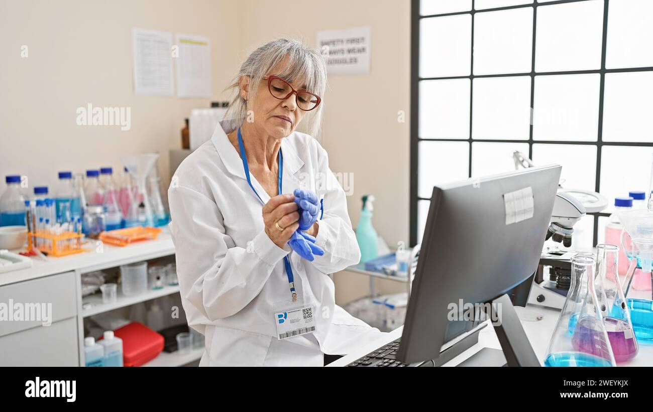 Mature woman scientist in lab coat analyzing data on computer amidst ...