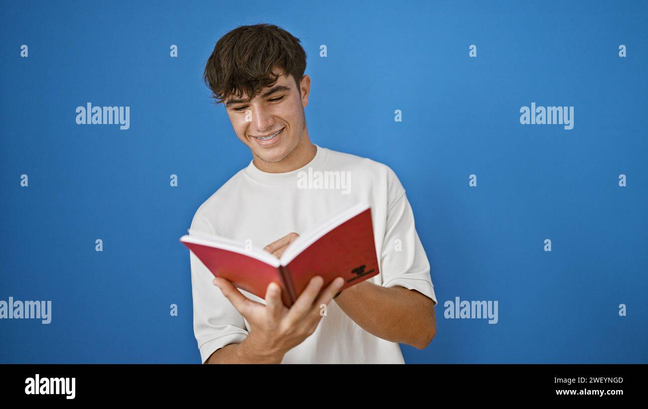 Confident young hispanic student, a teenager with a charming smile, casually standing and taking notes, relishing his studying hours, isolated over a Stock Photo