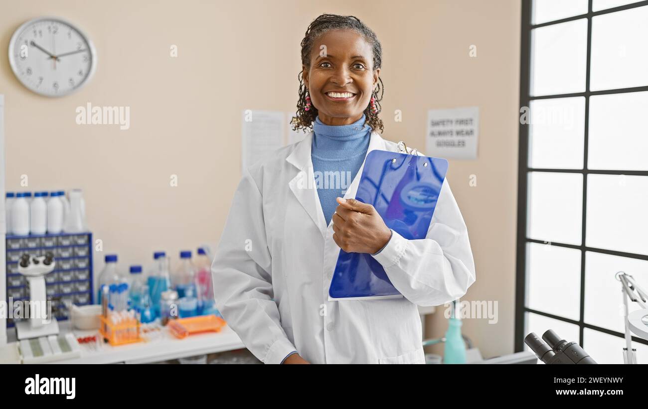 Happy african american woman scientist in lab coat with clipboard at ...