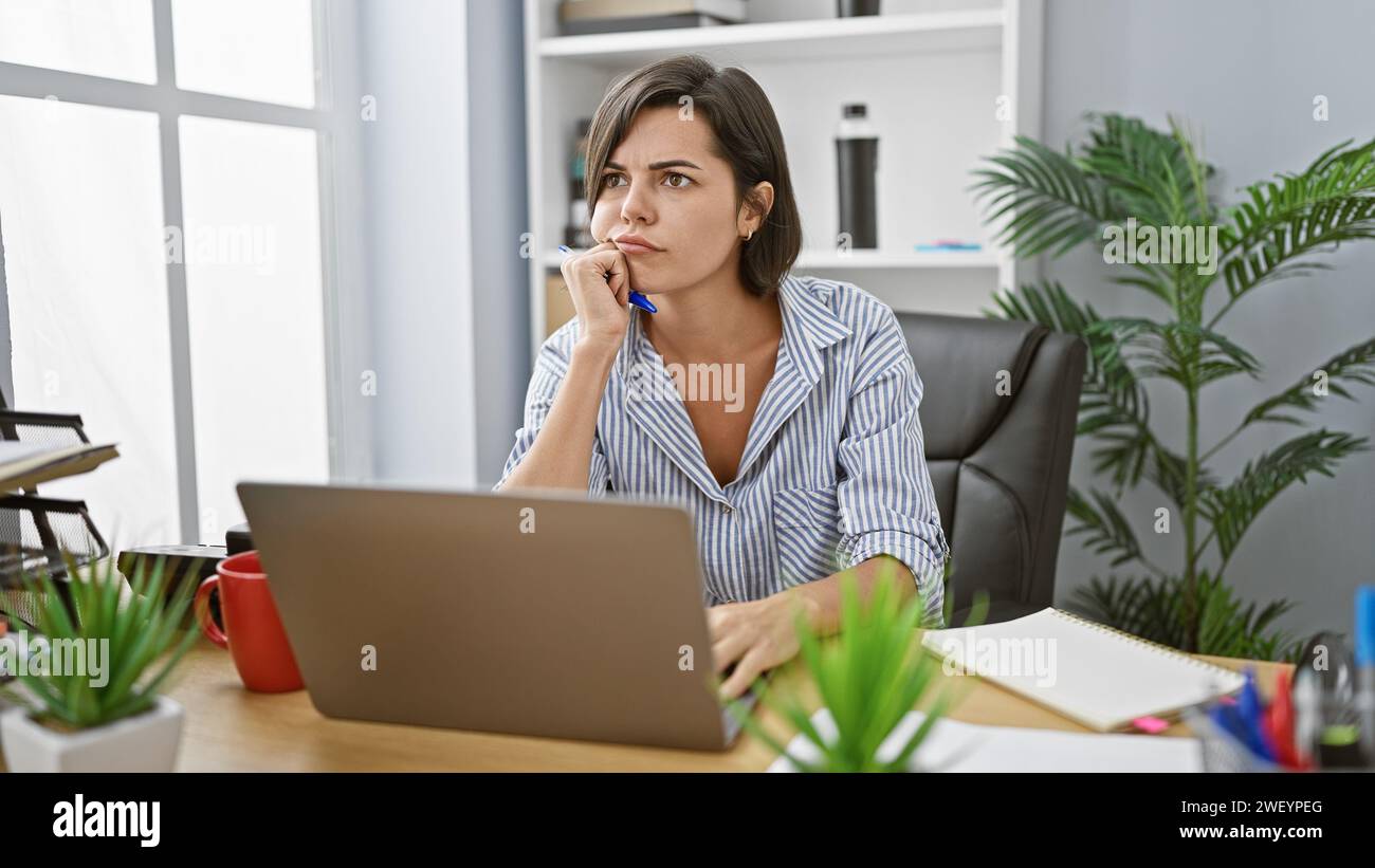 The portrait of a seriously relaxed, beautiful young hispanic woman worker, doubtfully thinking of her next big business idea while working online at Stock Photo