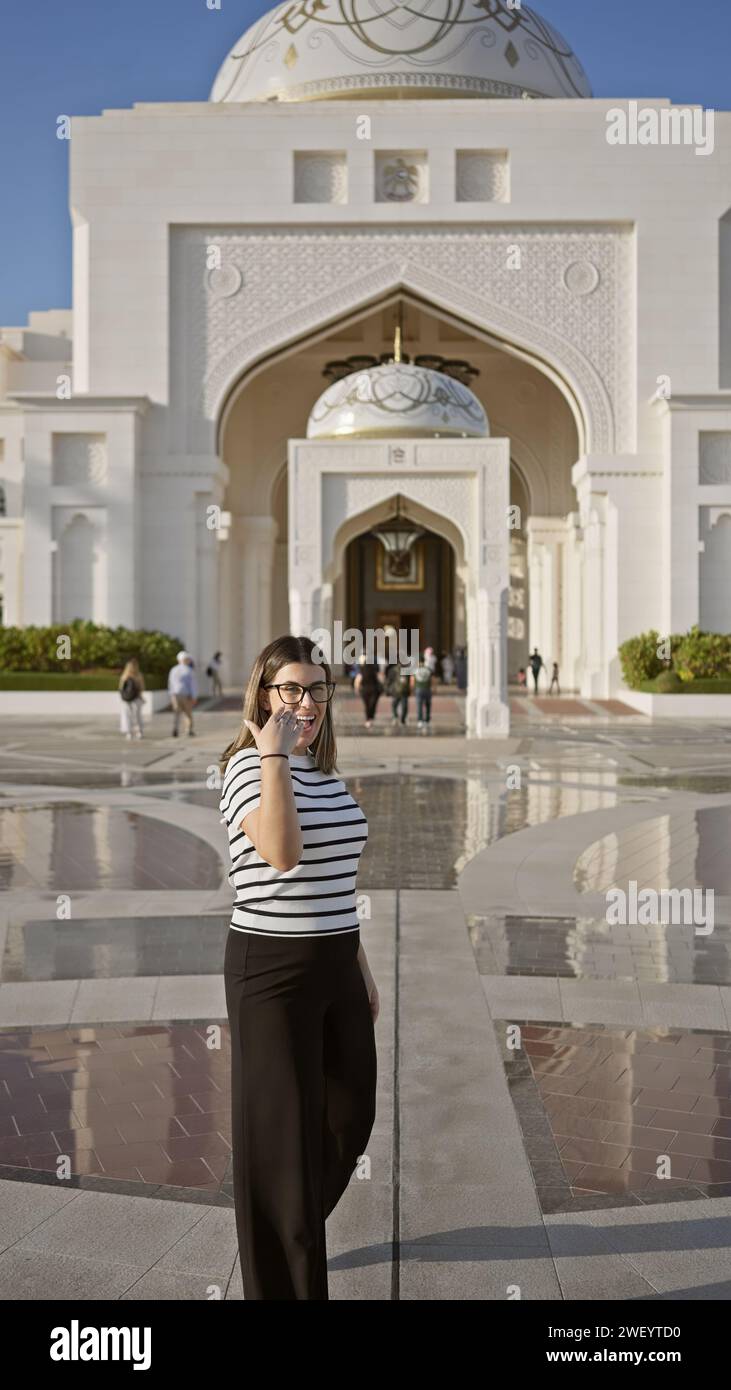 A smiling young woman in casual clothing stands before the majestic qasr al watan in abu dhabi. Stock Photo