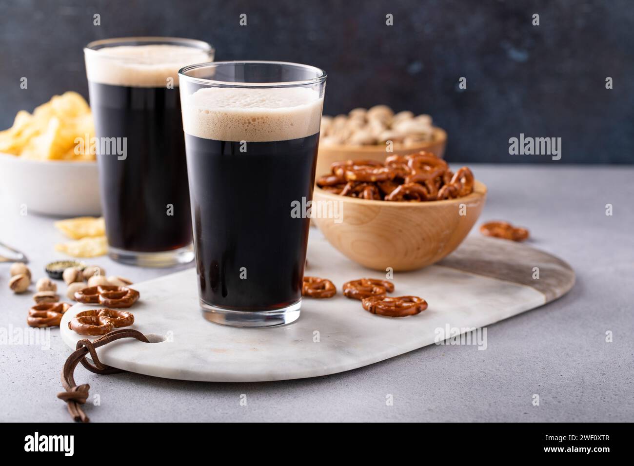 Dark stout beer in tall glasses with nuts, pretzels and chips Stock Photo