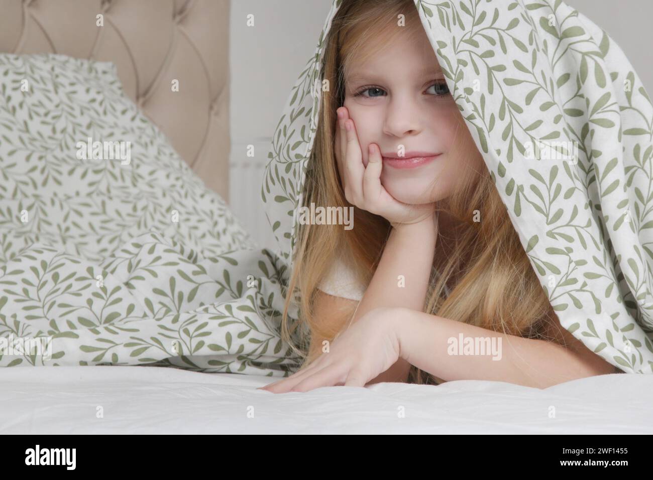 Adorable little preschool girl hiding under blanket, smilling and