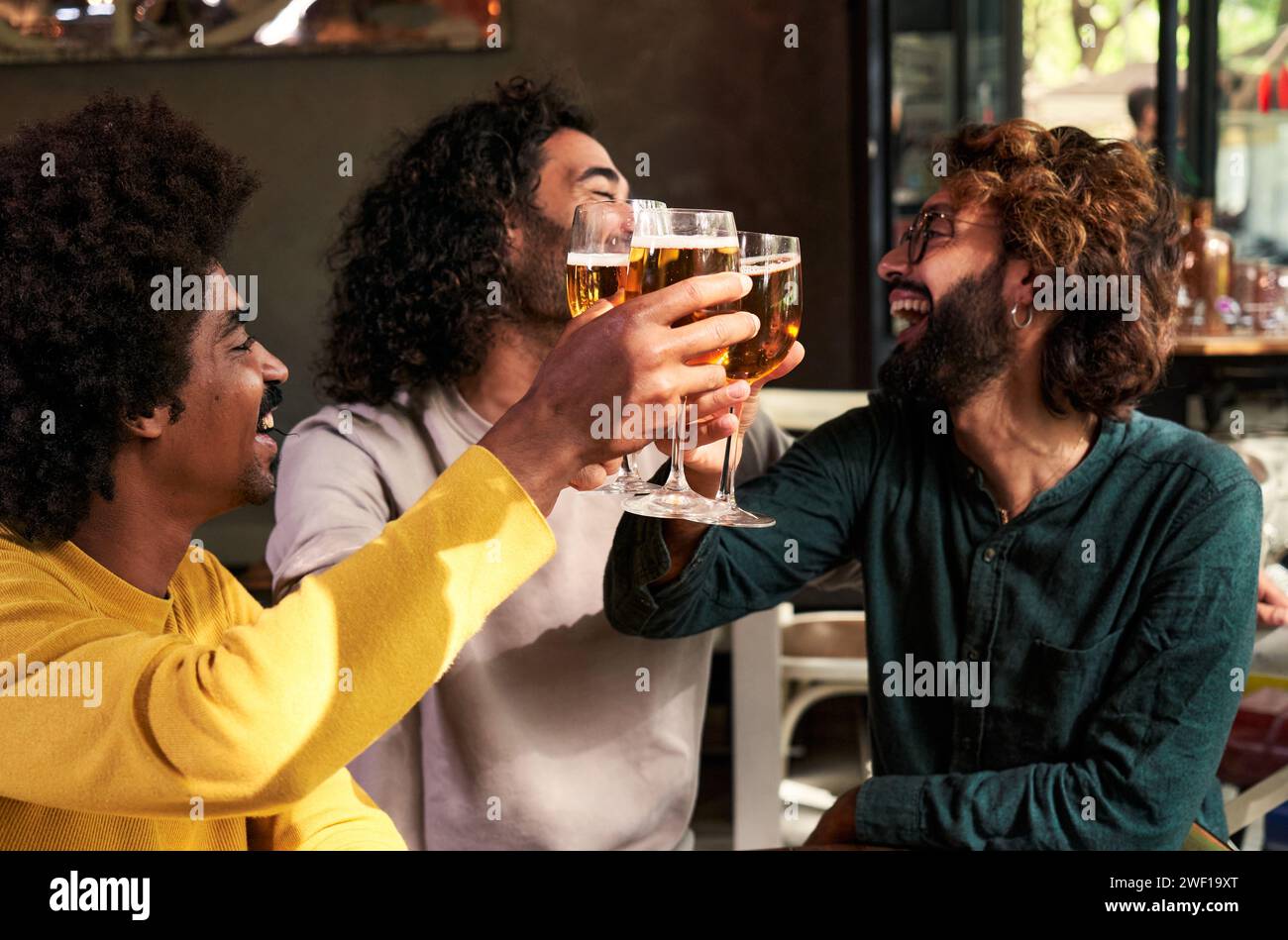 Small group of multiracial male friends toasting with beers together in a bar. Stock Photo